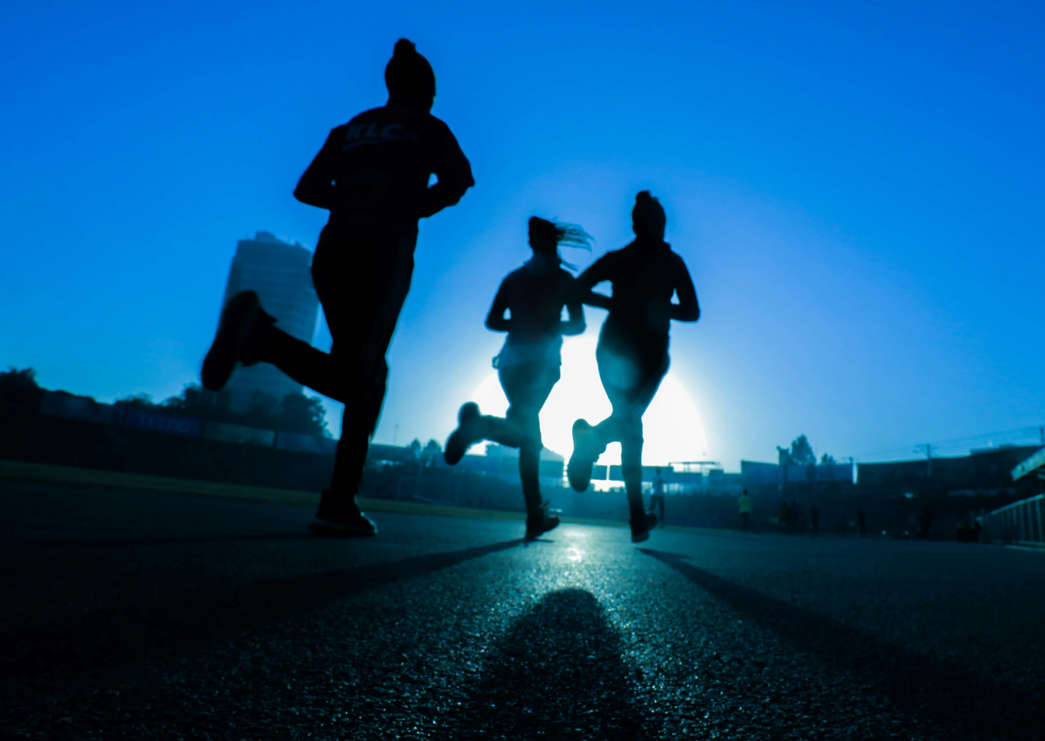 Three women running against an urban blue sky